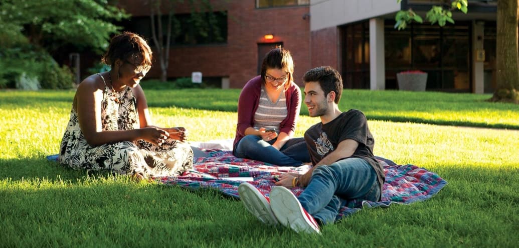 three students sit on grass