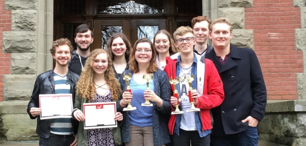 In this photo, the SPU debate team stands together smiling in front of a building.