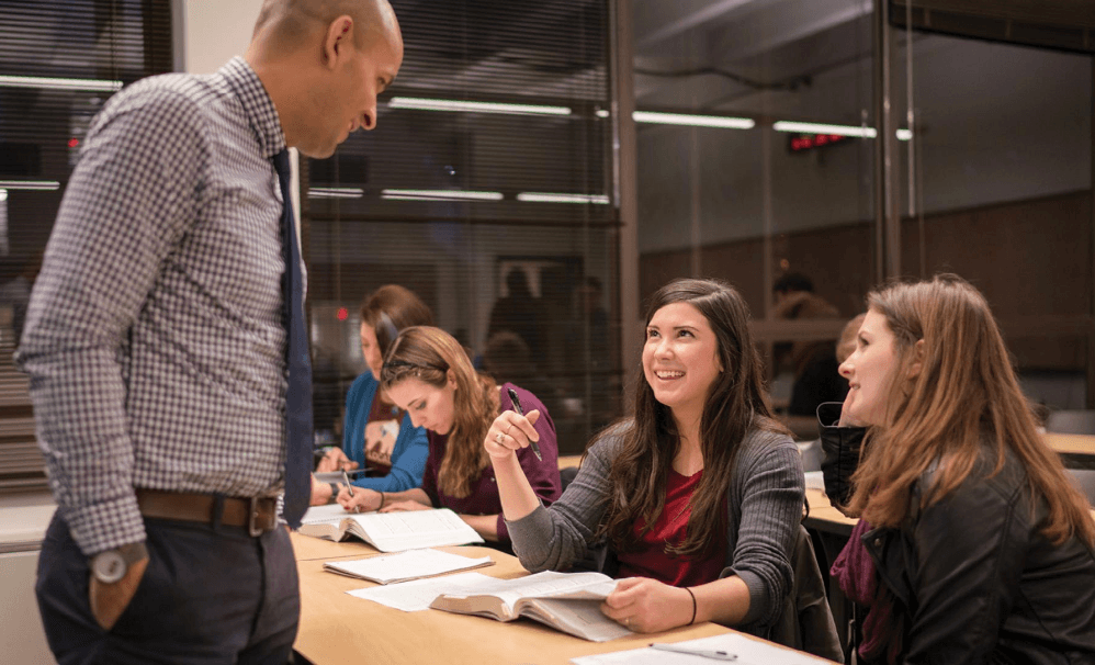 Professor standing at desk talking to students