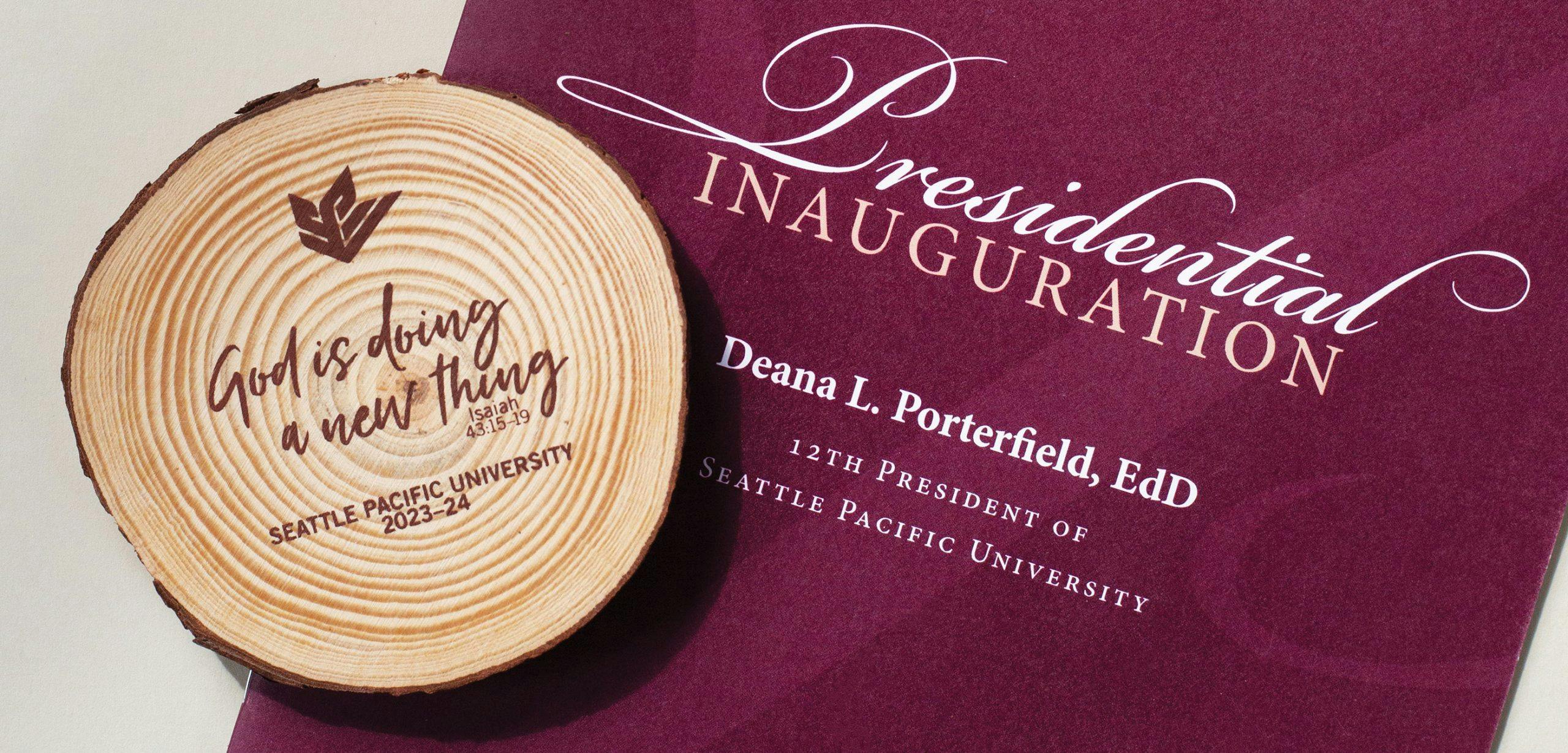 A wooden coaster sits on a program from Dr. Deana L. Porterfield's inauguration. The coaster reads "God is doing a new thing (Isaiah 43:15-19) Seattle Pacific University 2023-24