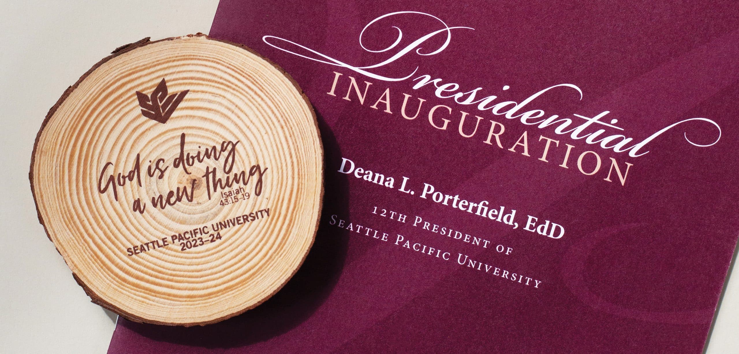 A wooden coaster sits on a program from Dr. Deana L. Porterfield's inauguration. The coaster reads "God is doing a new thing (Isaiah 43:15-19) Seattle Pacific University 2023-24