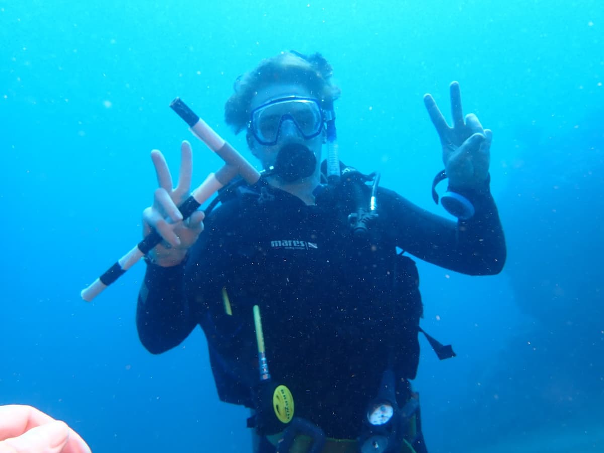 Student Weston Hanson gives the peace sign with both hands during an underwater scuba dive.