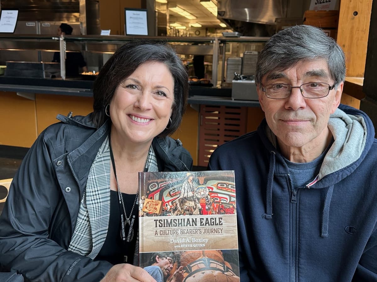 SPU President Porterfield sits next to SPU alumnus David Boxley. She is holding a autobiography David presented to the SPU library.