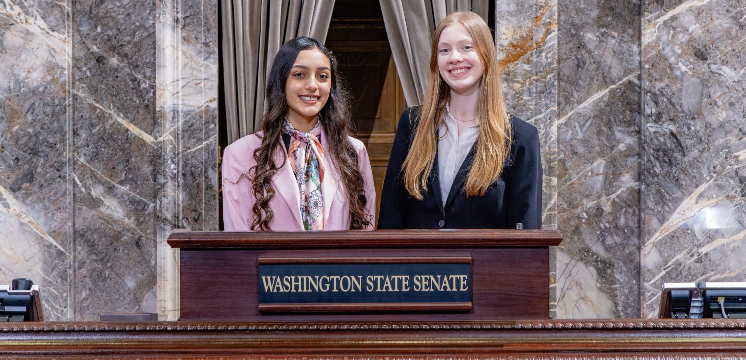 Karla and Sadie at a podium with Washington State Senate underneath. Courtesy of Washington state Legislature.