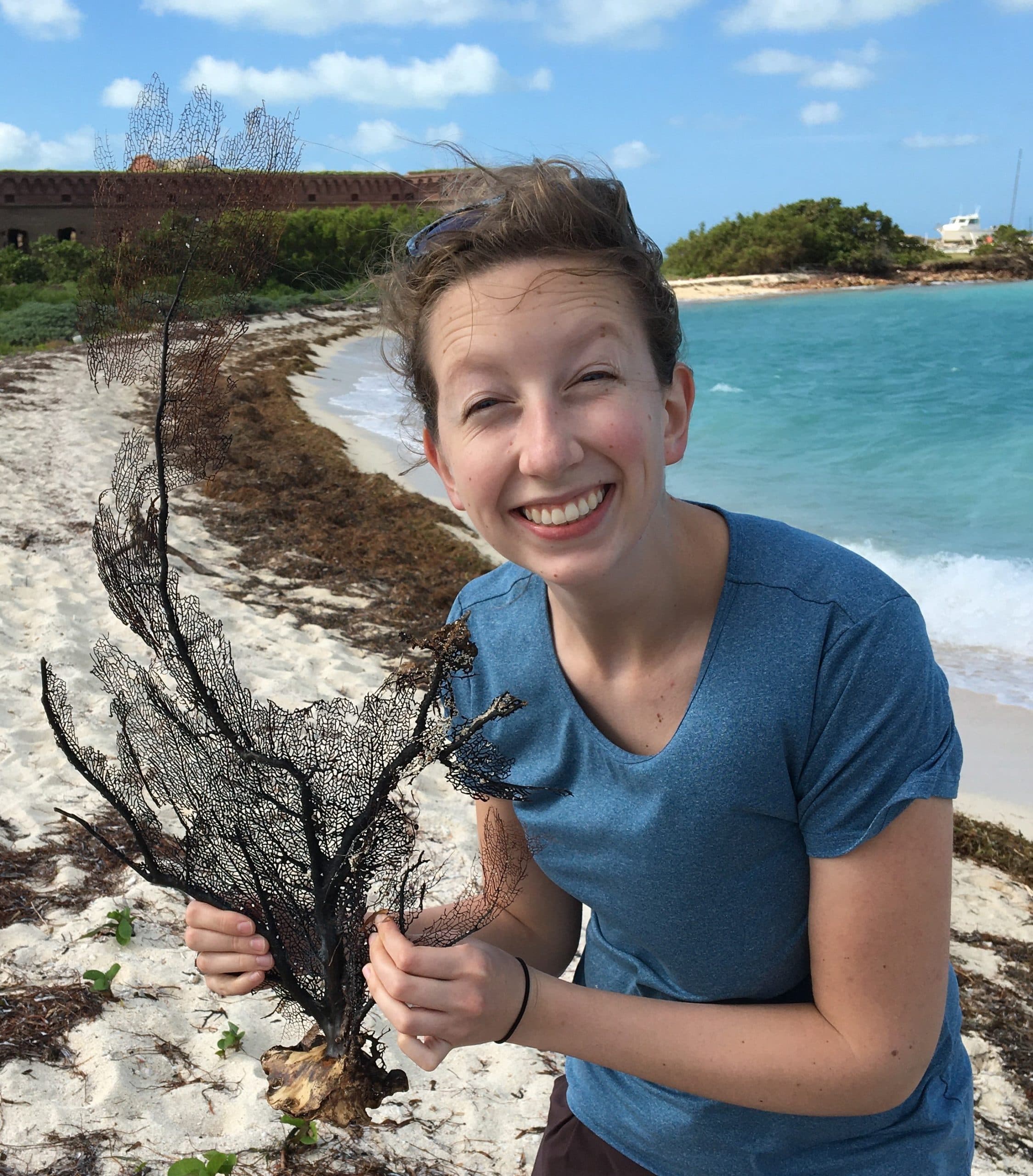 Rachel Jordan holding a piece of coral on a beach.