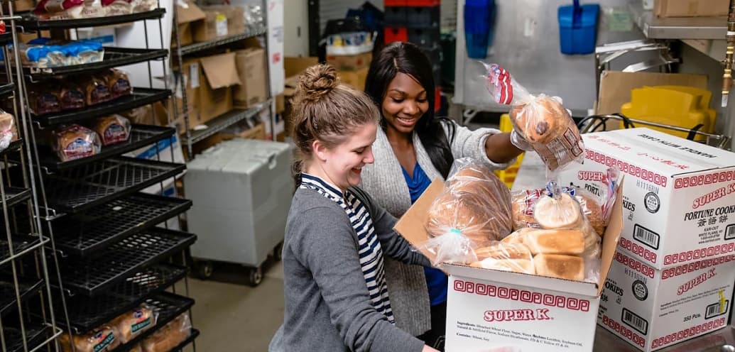 Lauren Isham and Maya Swinehart in Gwinn Commons packing food for the homeless.