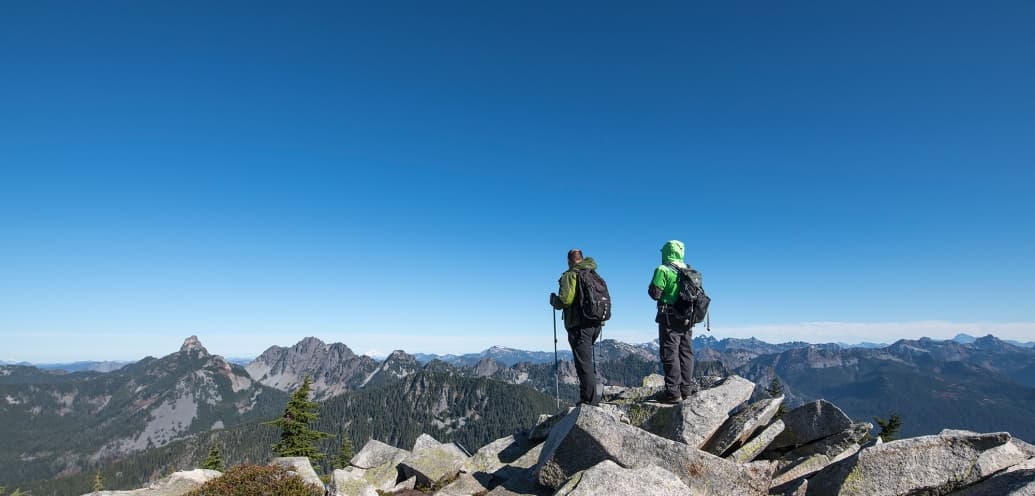 Two people look across mountains from a mountaintop.