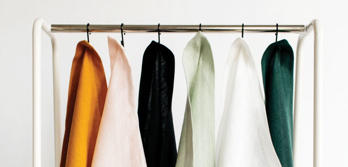 A variety of fabrics hang from a rack against a white wall photo by Brittney Hyatt
