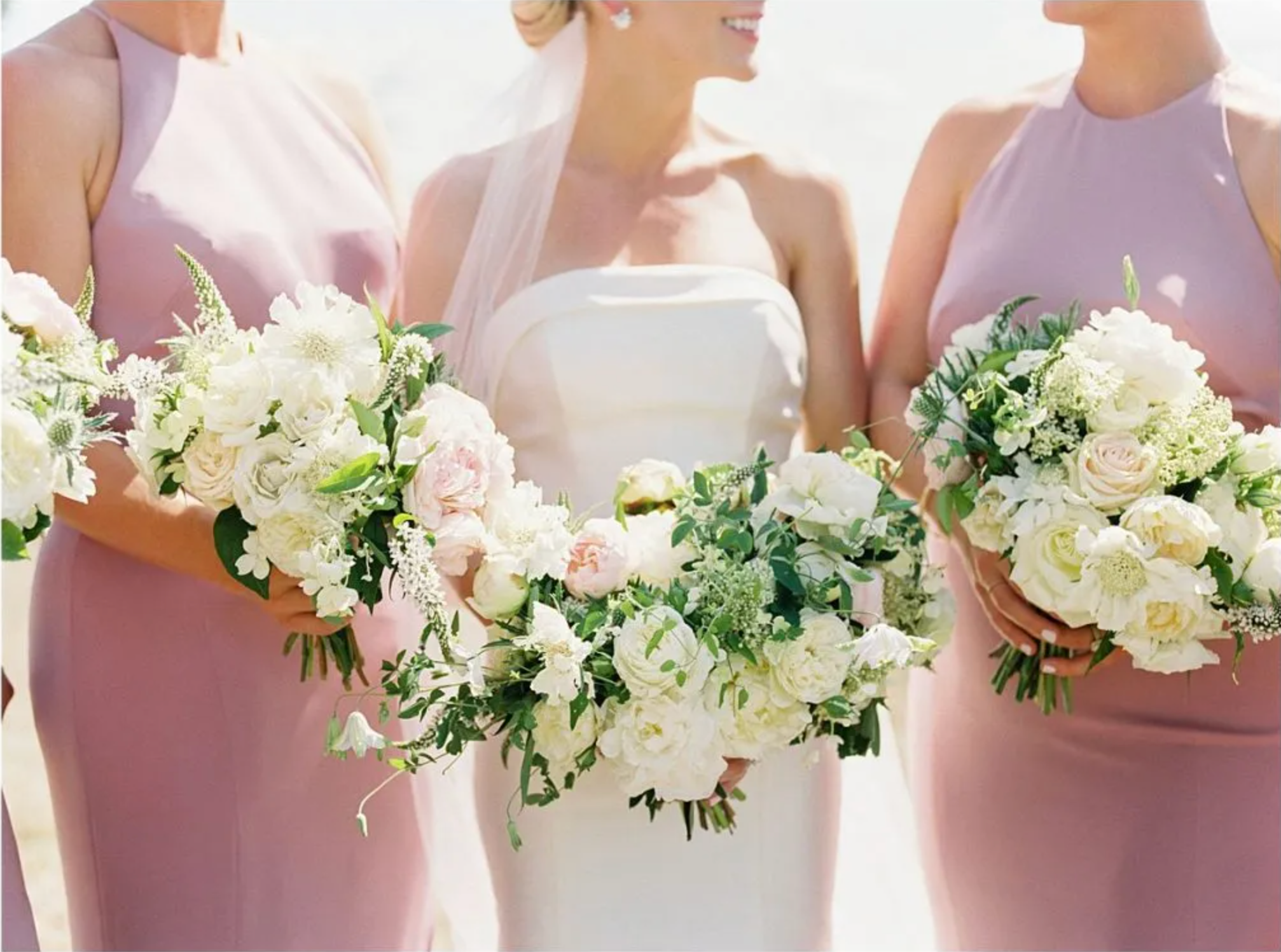 Half body shot of bride in the center with two bridesmaids in pink on either side with everyone holding bouquets of flowers