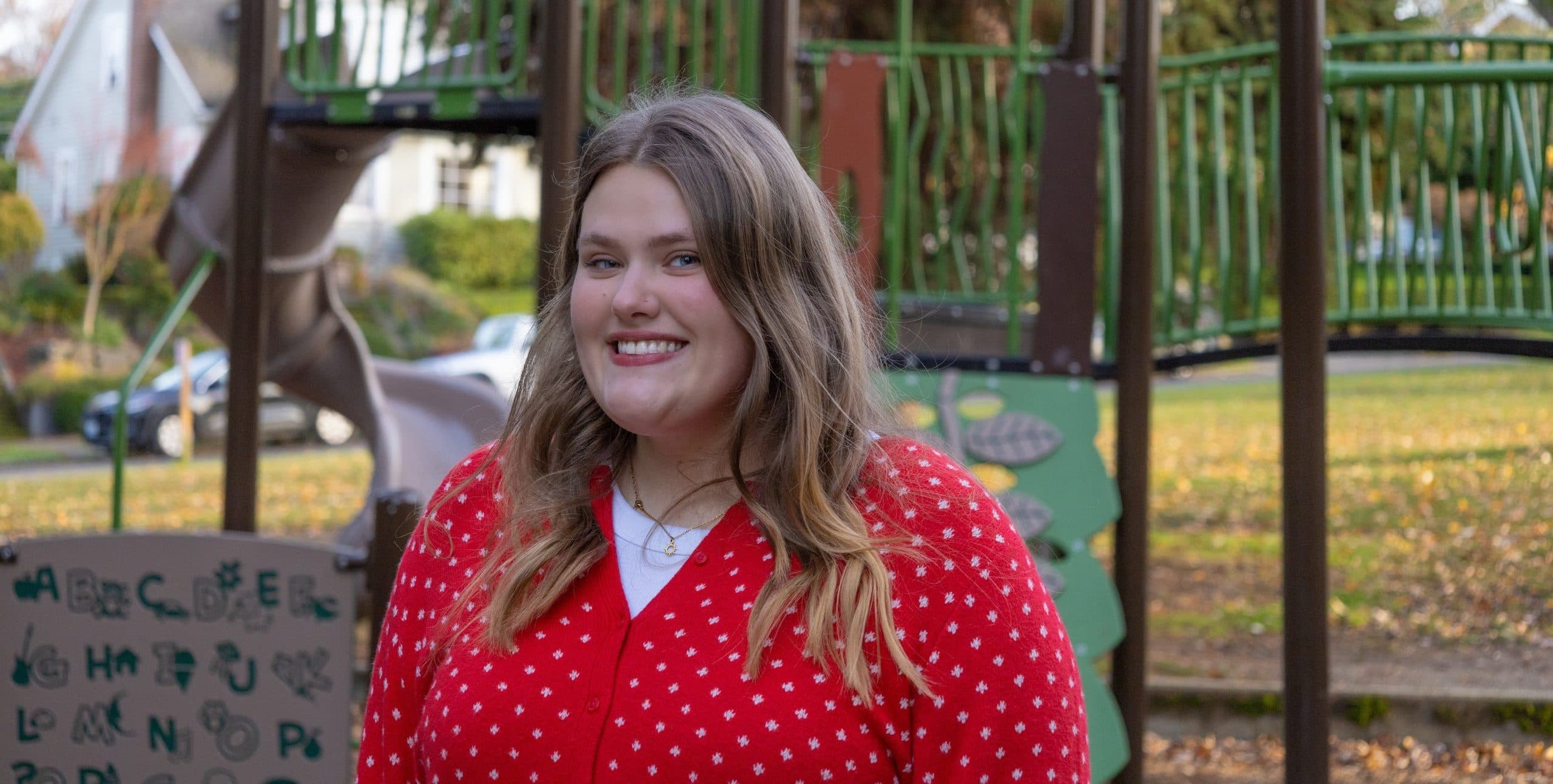 alumna Ky Krogh in red sweater in front of playground equipment at park