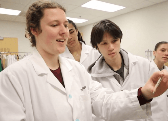 Students in white lab coats look at a slide.