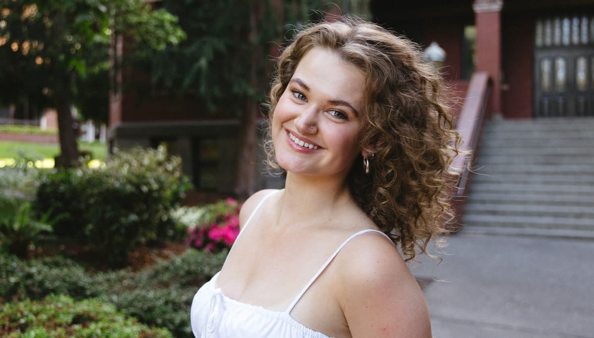 Emily Graves in a white dress in front of the steps of Peterson Hall.